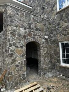 the image shows a stone archway entrance under construction for a custom home highlighting natural stonework and architectural design