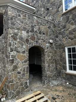 the image shows a stone archway entrance under construction for a custom home highlighting natural stonework and architectural design